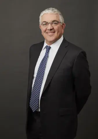 Eric Stamps in front of a grey background wearing dark suit and patterned tie.