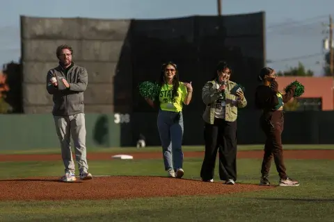 SMU College of Nursing Dean Steven Rush prepares to throw the ceremonial first pitch alongside event staff and hosts on the pitcher’s mound.