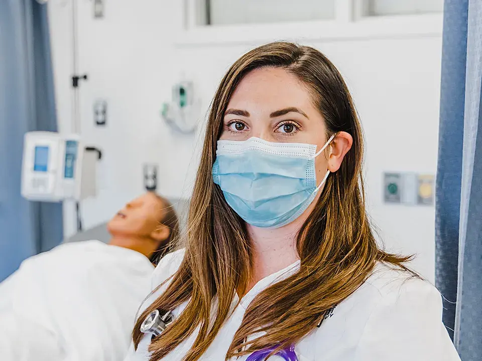 RN to BSN nursing student in simulation lab with manikin behind.